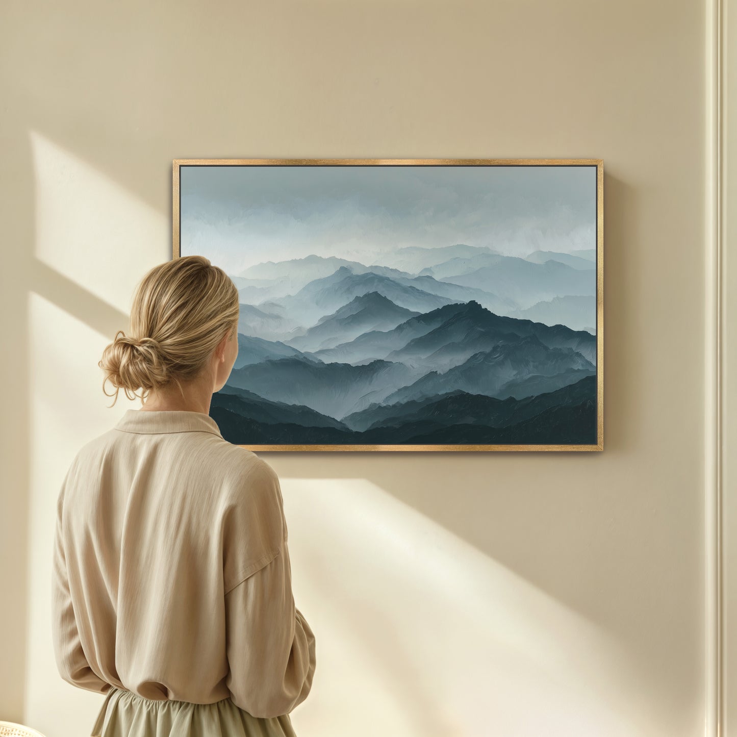 A woman stands in front of a framed landscape painting, gazing at the mountains depicted in the artwork.