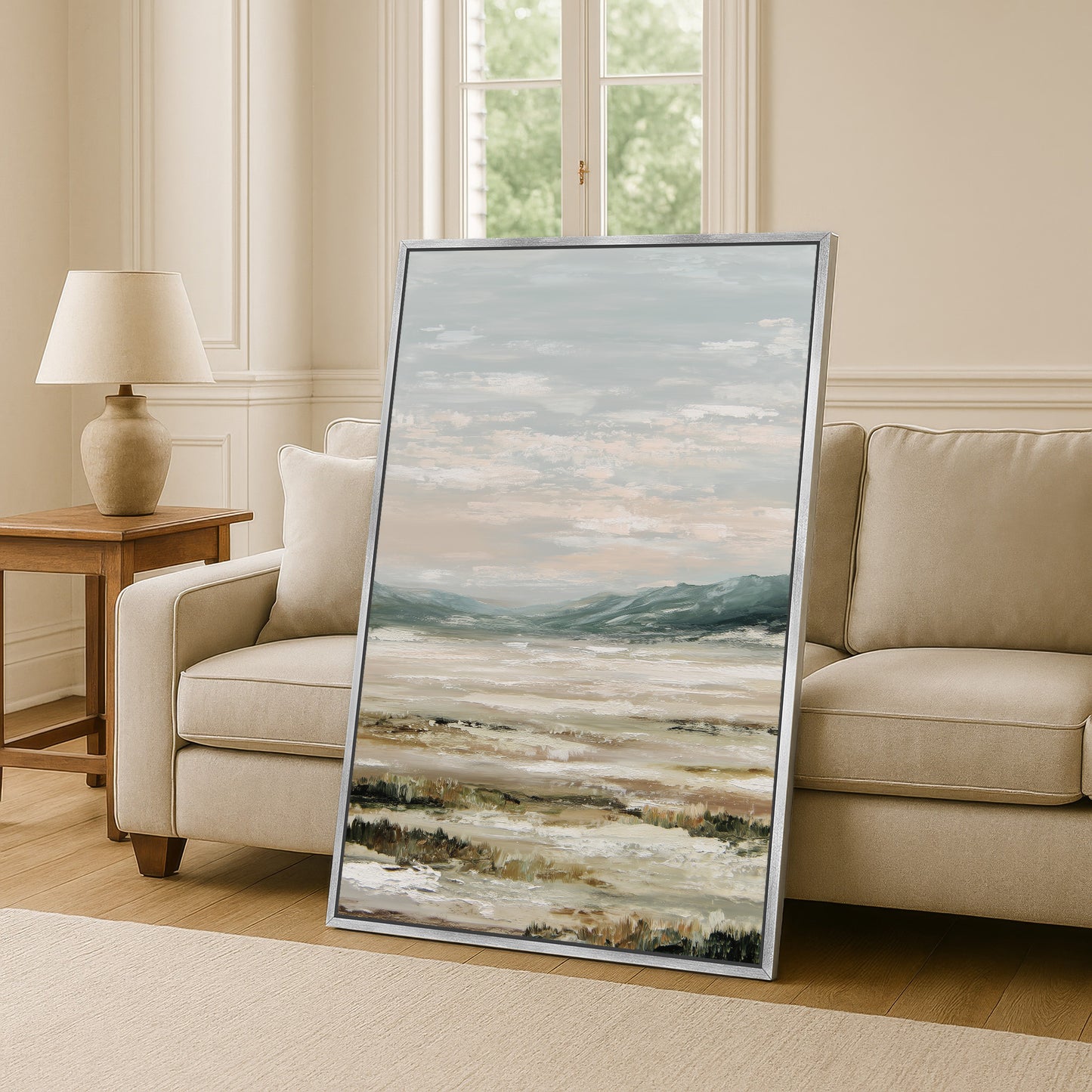 a large landscape painting displayed on a wall in a living room, with a beige sofa and a wooden side table visible in the background.