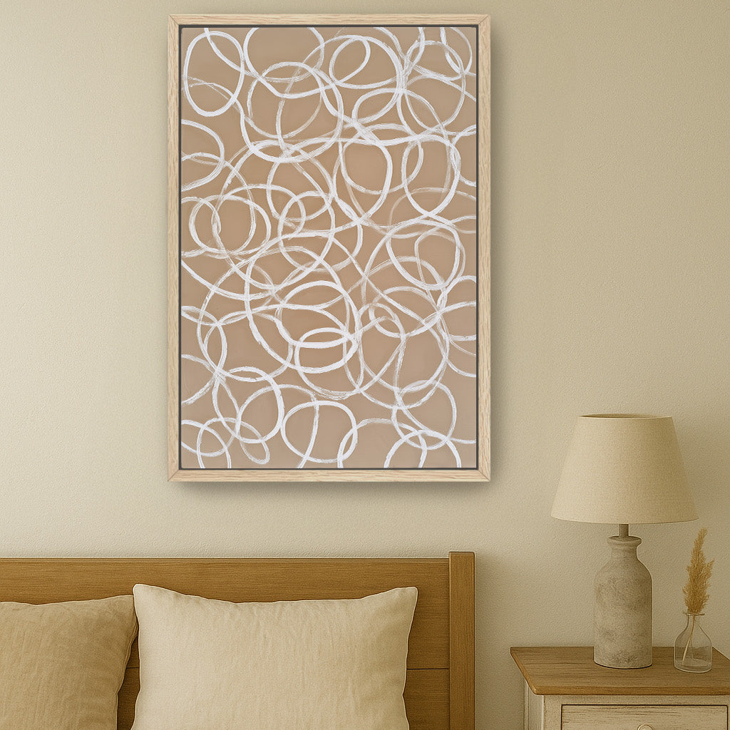 a bedroom with a bed, a nightstand, and a lamp. The bed has a wooden headboard and is covered with a beige comforter. Above the bed, there is a framed artwork with a repeating pattern of white circles on a beige background.