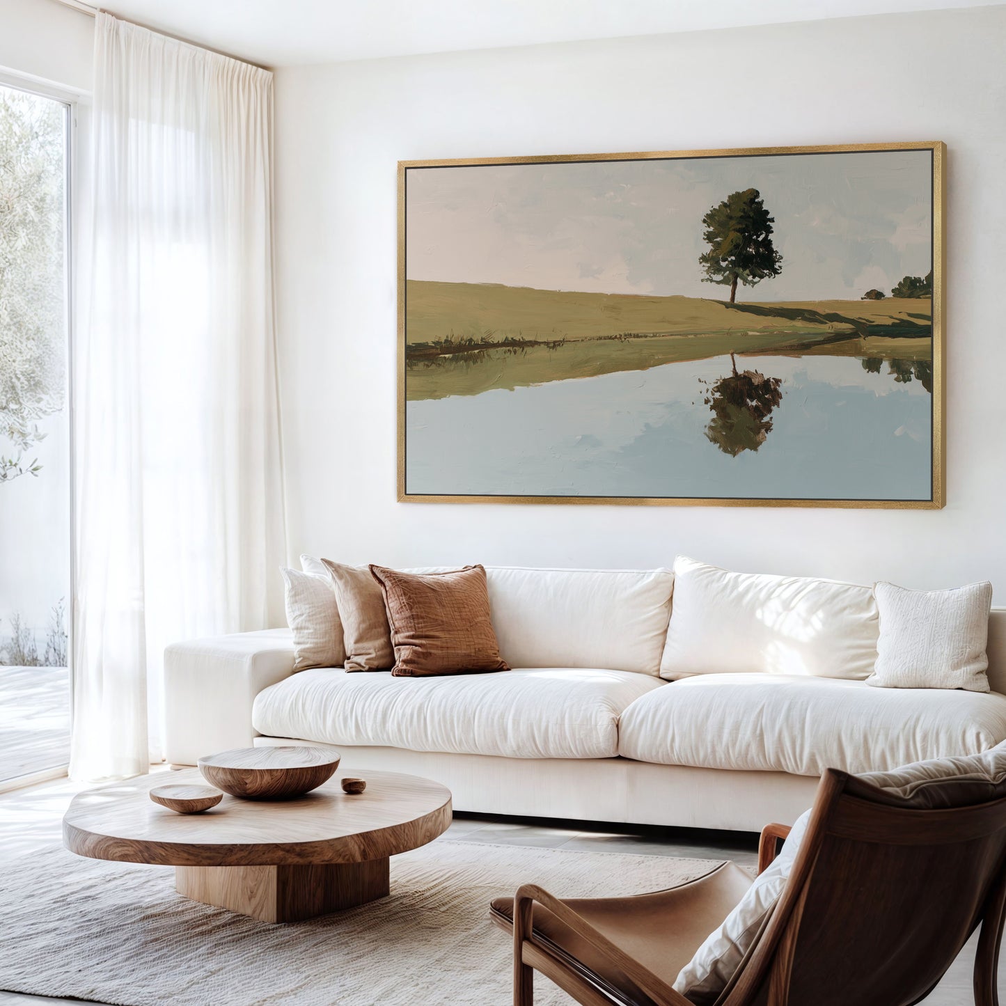 a serene living room with a large painting of a tree and a lake on the wall, a white sofa, a wooden coffee table, and a brown leather armchair.