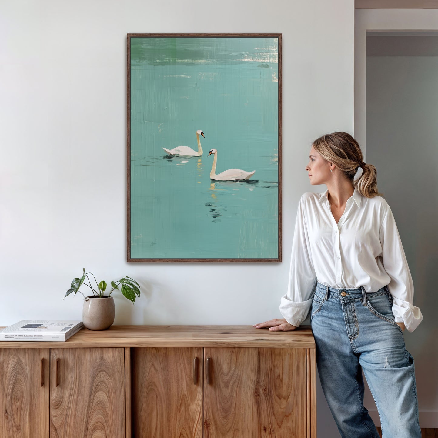 Modern Evara swan lake artwork displayed beside woman in natural wood room, minimalist coastal wall art.