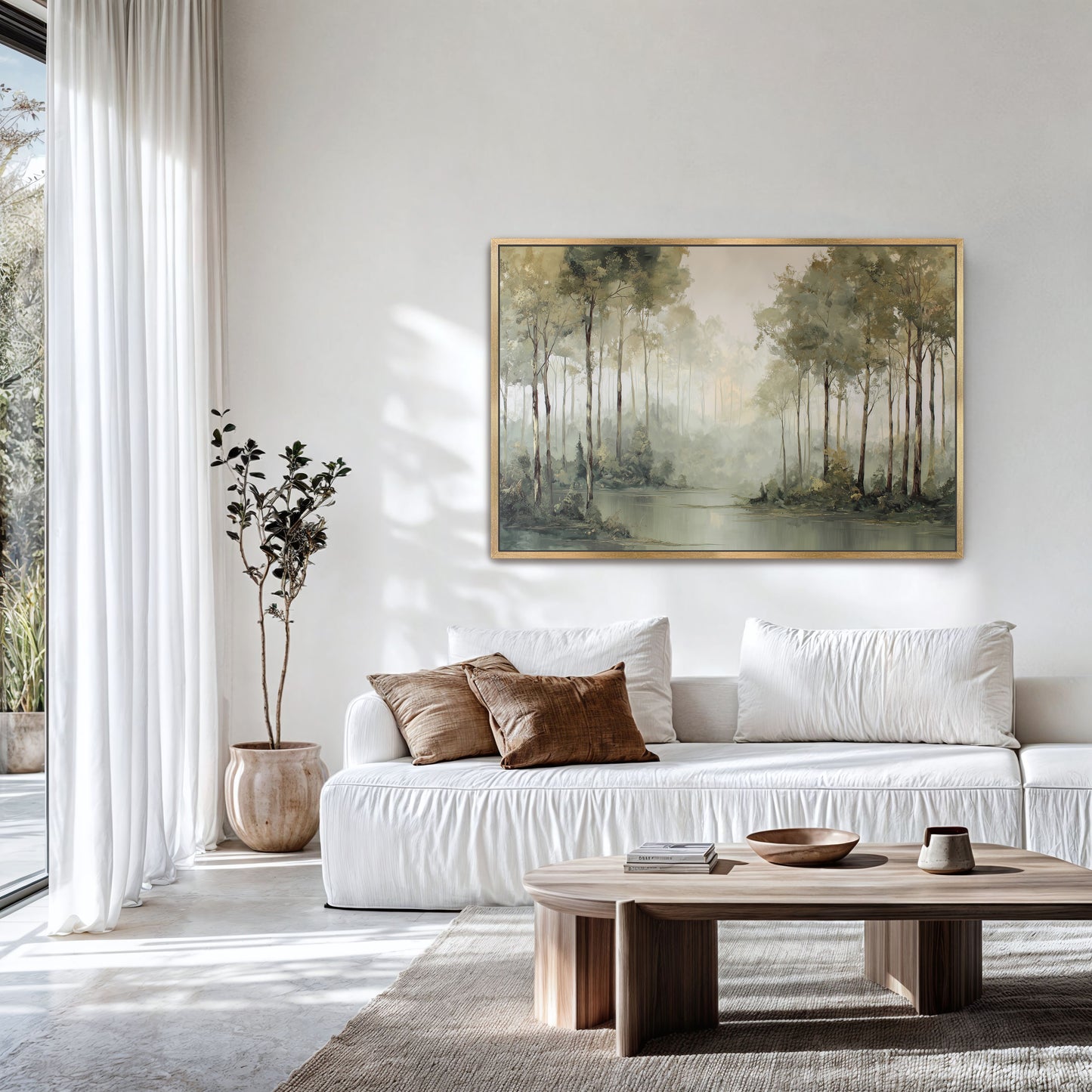 Misty forest edge landscape print in a natural frame above a white sofa in a light-filled room.