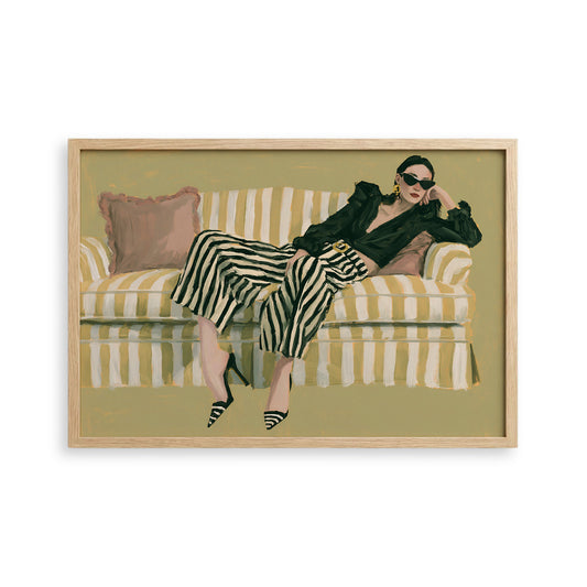 A woman is sitting on a striped couch, wearing a black jacket and striped pants, with her legs crossed and her head resting on her hand.