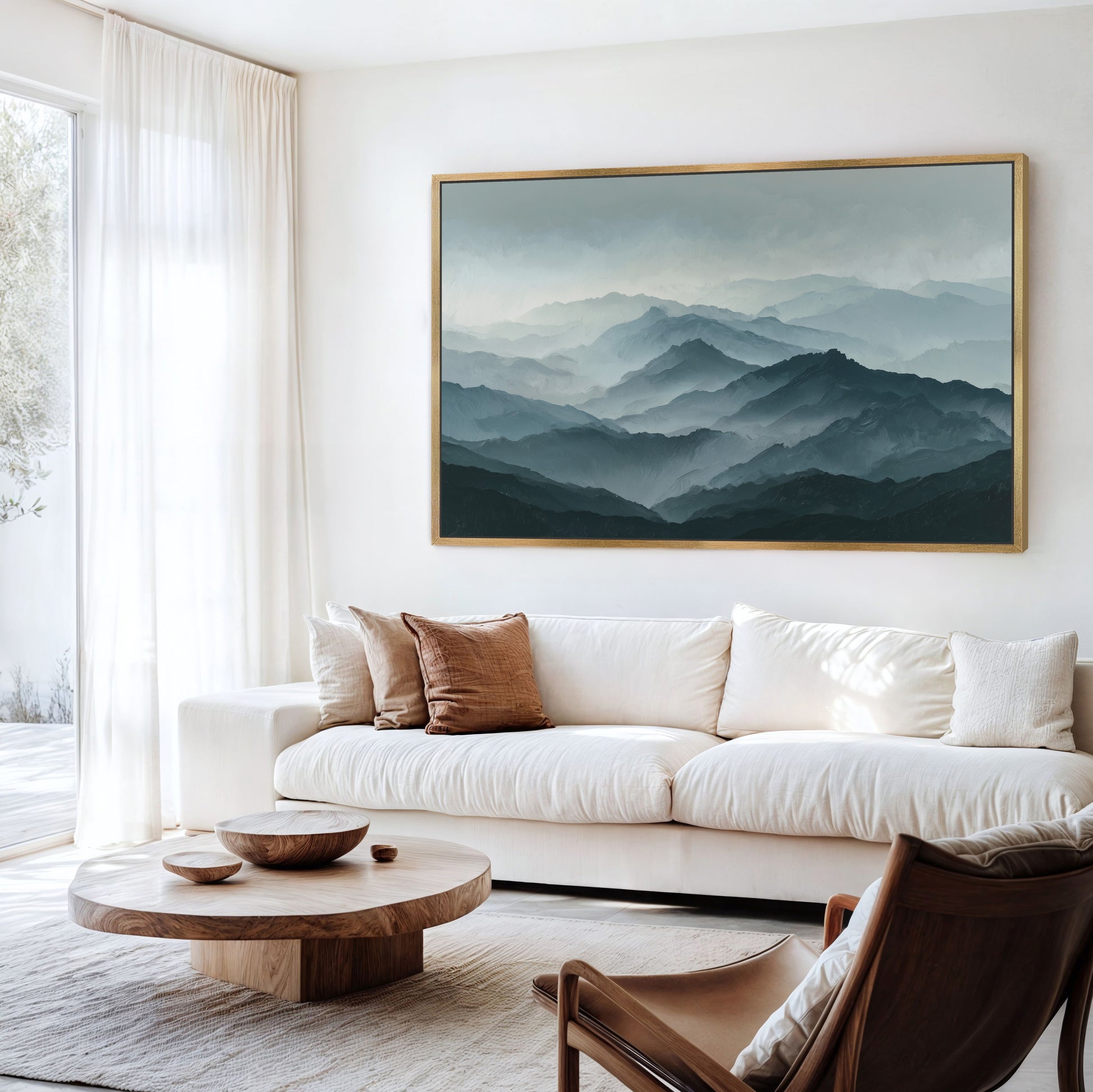 a serene living room with a large framed landscape painting hanging on the wall, depicting a mountainous scene with a hazy, misty atmosphere. The room is furnished with a white sofa, a wooden coffee table, and a brown leather armchair, creating a cozy and inviting atmosphere.