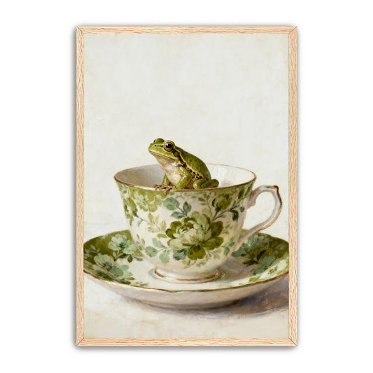 A green frog sits in a teacup with a matching floral pattern, set on a matching saucer.