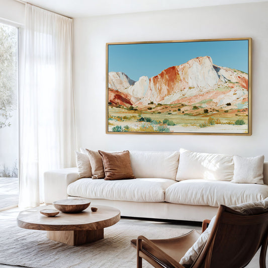 a living room with a large, colorful painting of a mountain landscape hanging on the wall above a white sofa. The sofa is positioned in front of a wooden coffee table, and a brown leather armchair is located nearby. The room has a bright and airy atmosphere, with natural light coming in through a window.