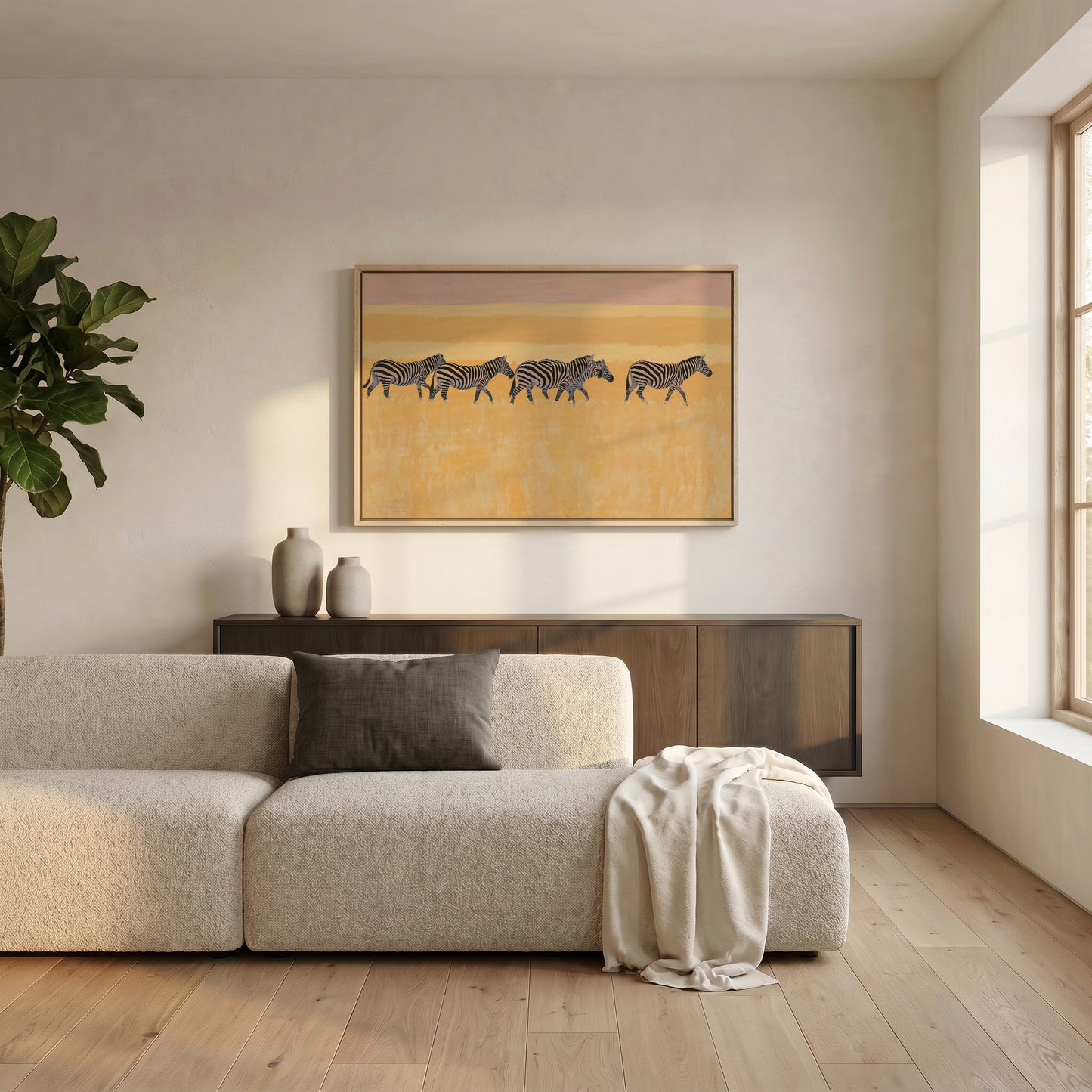 a modern living room with a large, beige sofa and a wooden coffee table. Above the sofa, there is a framed artwork of zebras on a yellow background. The room has a minimalist and clean design, with a large window providing natural light and a potted plant adding a touch of greenery.