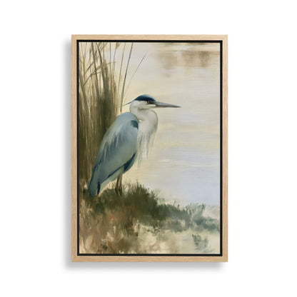 A blue heron standing on the bank of a body of water, surrounded by tall grasses.
