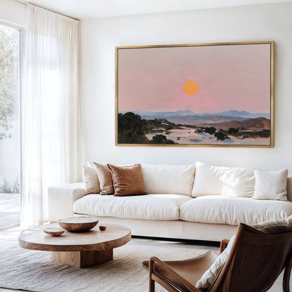 a living room with a large painting of a sunset landscape hanging on the wall above a white sofa. The sofa is positioned in front of a wooden coffee table, which has a bowl and a vase on it. There is also a chair in the room.