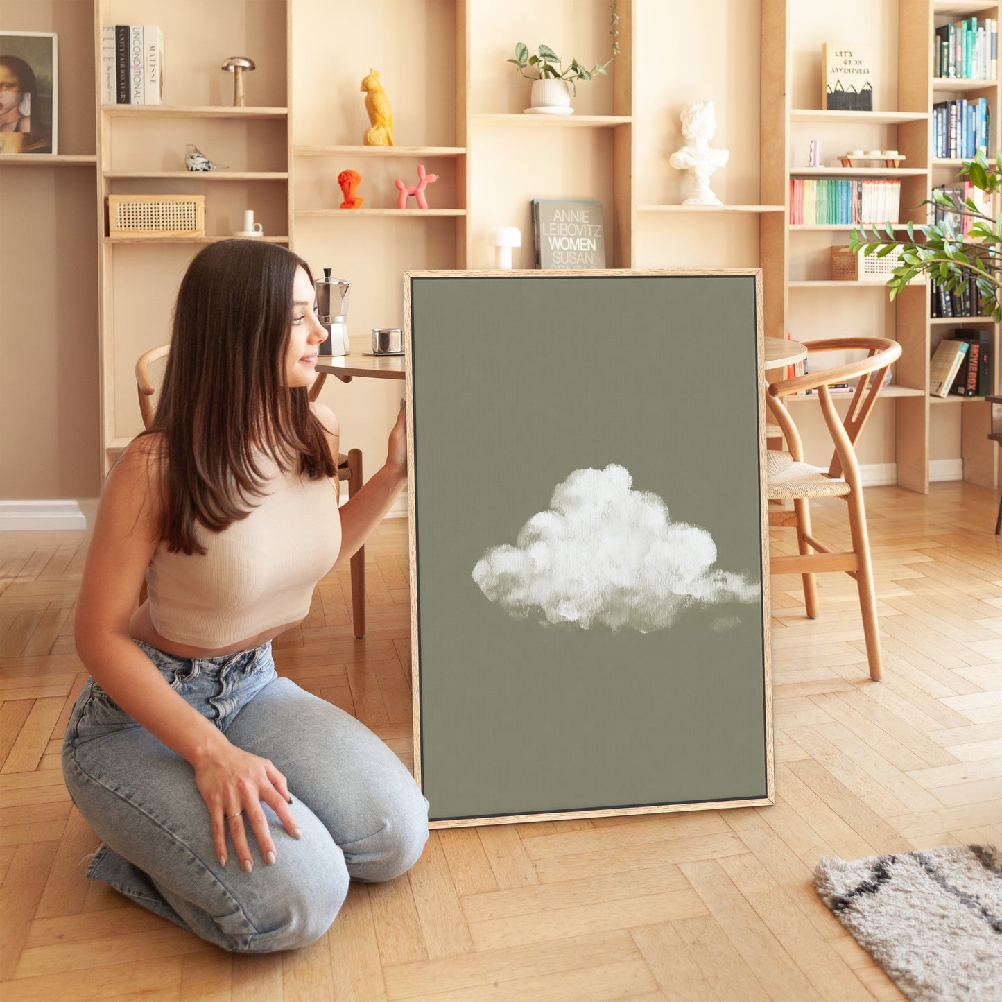 Woman displaying "Trace" canvas print featuring single white cloud on muted sage background in modern living room
