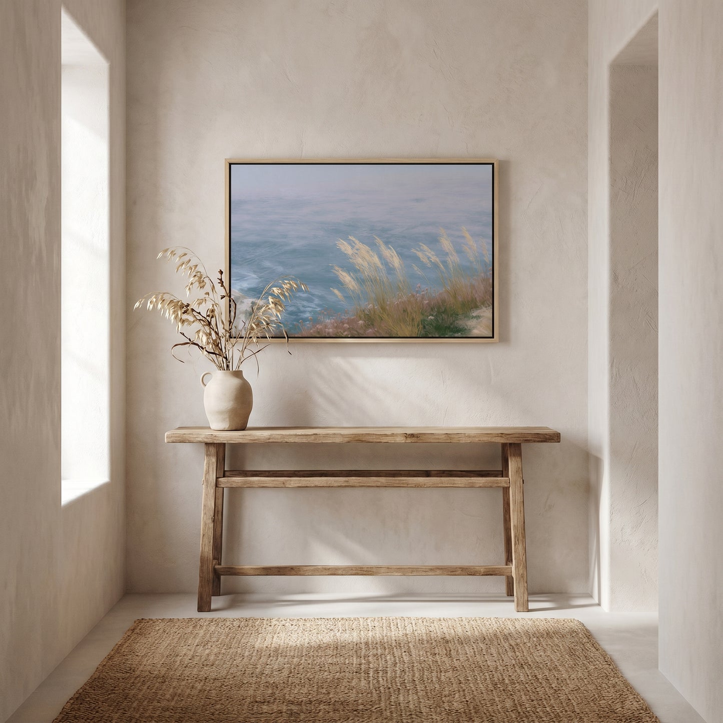 a serene indoor setting with a wooden console table, a vase of dried flowers, and a framed painting of a tranquil landscape above it.