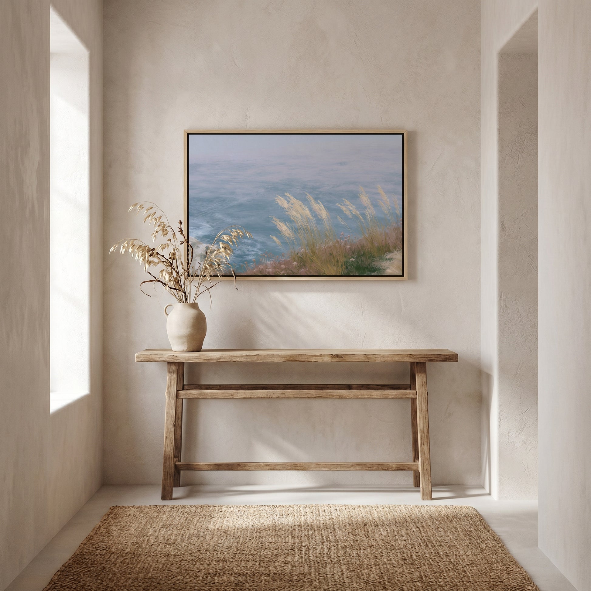 a serene indoor setting with a wooden console table, a vase of dried flowers, and a framed painting of a tranquil landscape above it.
