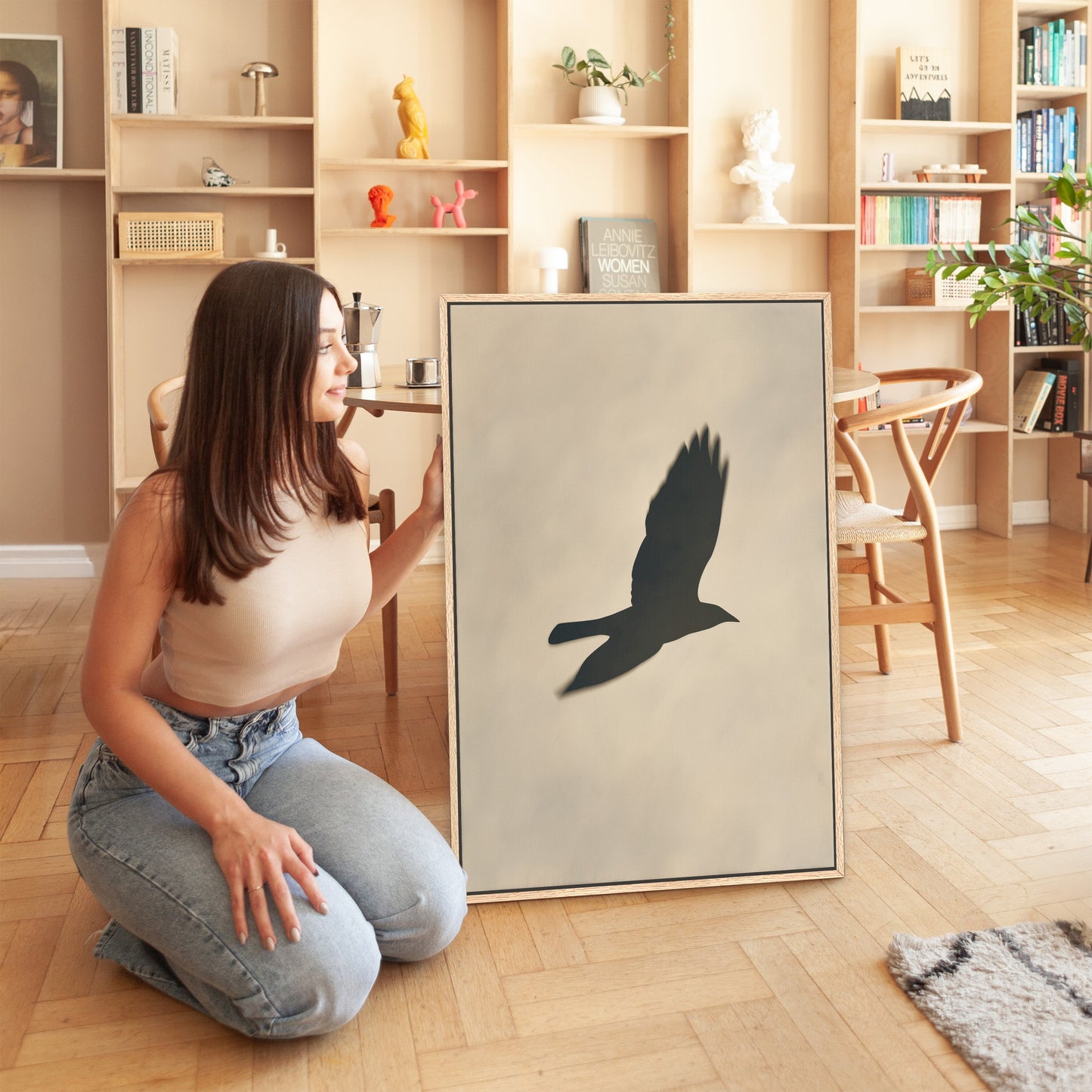 Woman kneeling beside Soar canvas print featuring bird silhouette in soft neutral light in modern interior