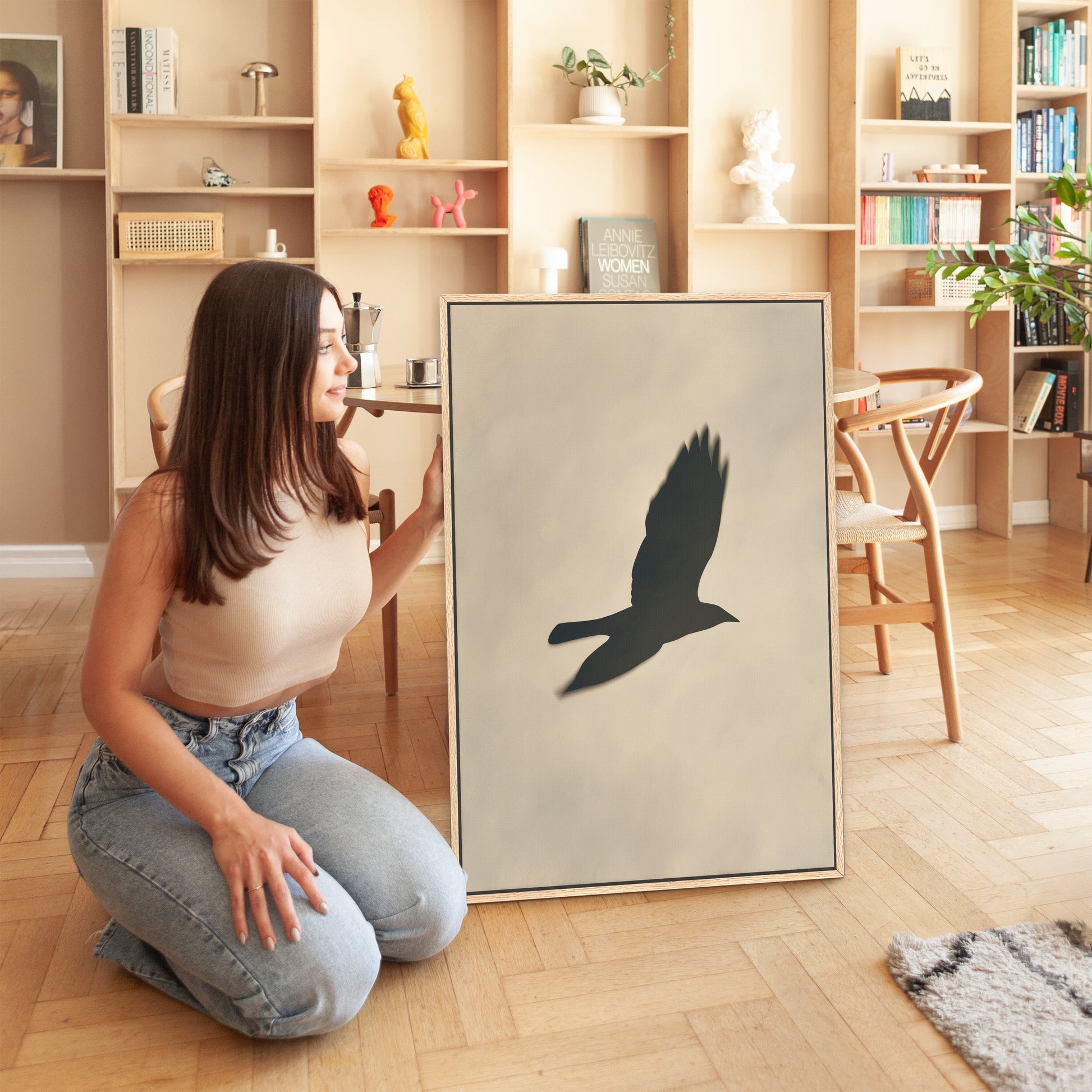 Woman kneeling beside Soar canvas print featuring bird silhouette in soft neutral light in modern interior