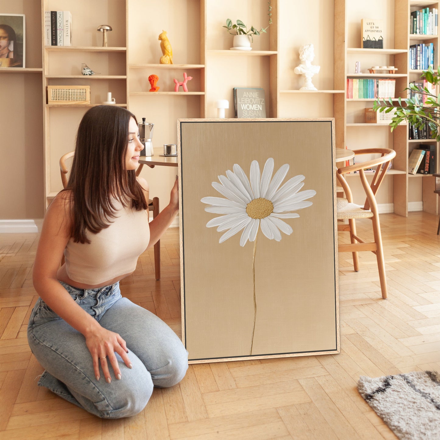 Woman kneeling beside Bloom canvas print featuring single white daisy on golden-beige background in modern living room