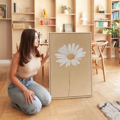 Woman kneeling beside Bloom canvas print featuring single white daisy on golden-beige background in modern living room