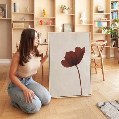 Woman kneeling next to "Stem" canvas print featuring a burgundy flower on neutral background in modern interior