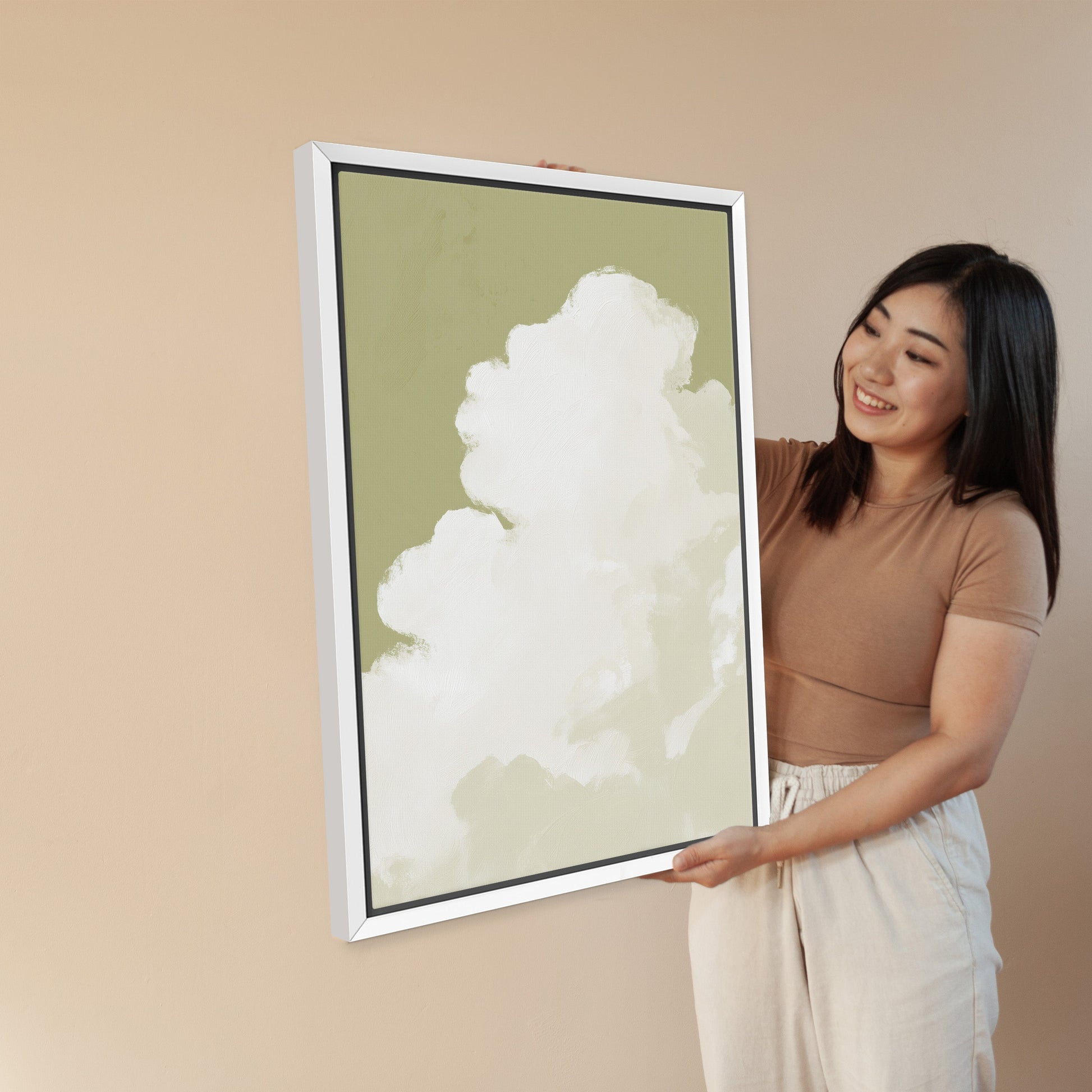 Woman holding Rise Canvas Wall Art featuring a white cloud on muted sage background in a white frame