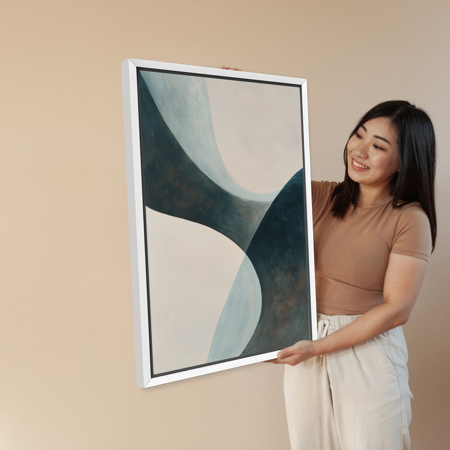 Woman holding 'Bend' canvas artwork with teal and cream abstract curves in white frame