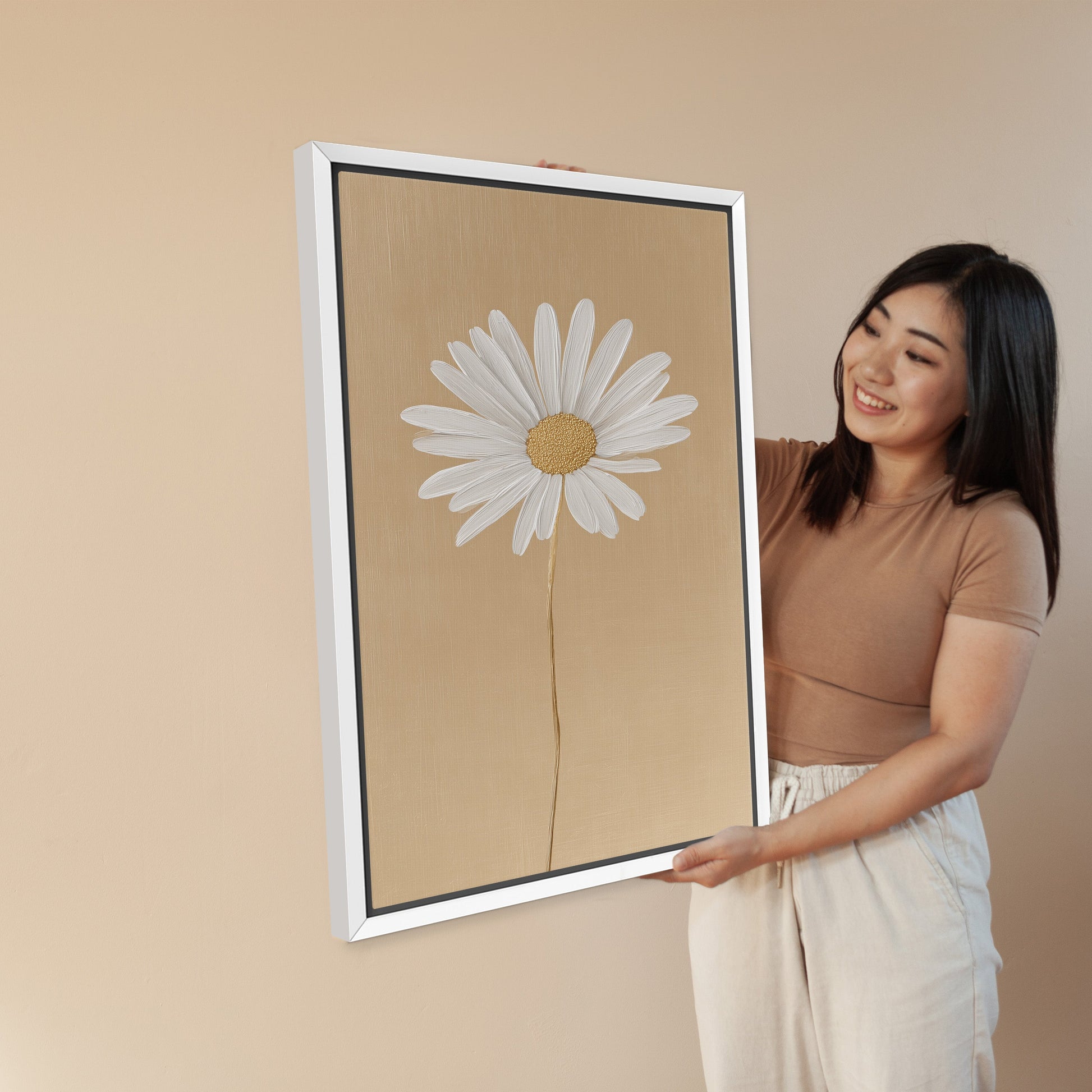 Woman holding 'Bloom' canvas print featuring single white daisy on golden-beige background in white frame