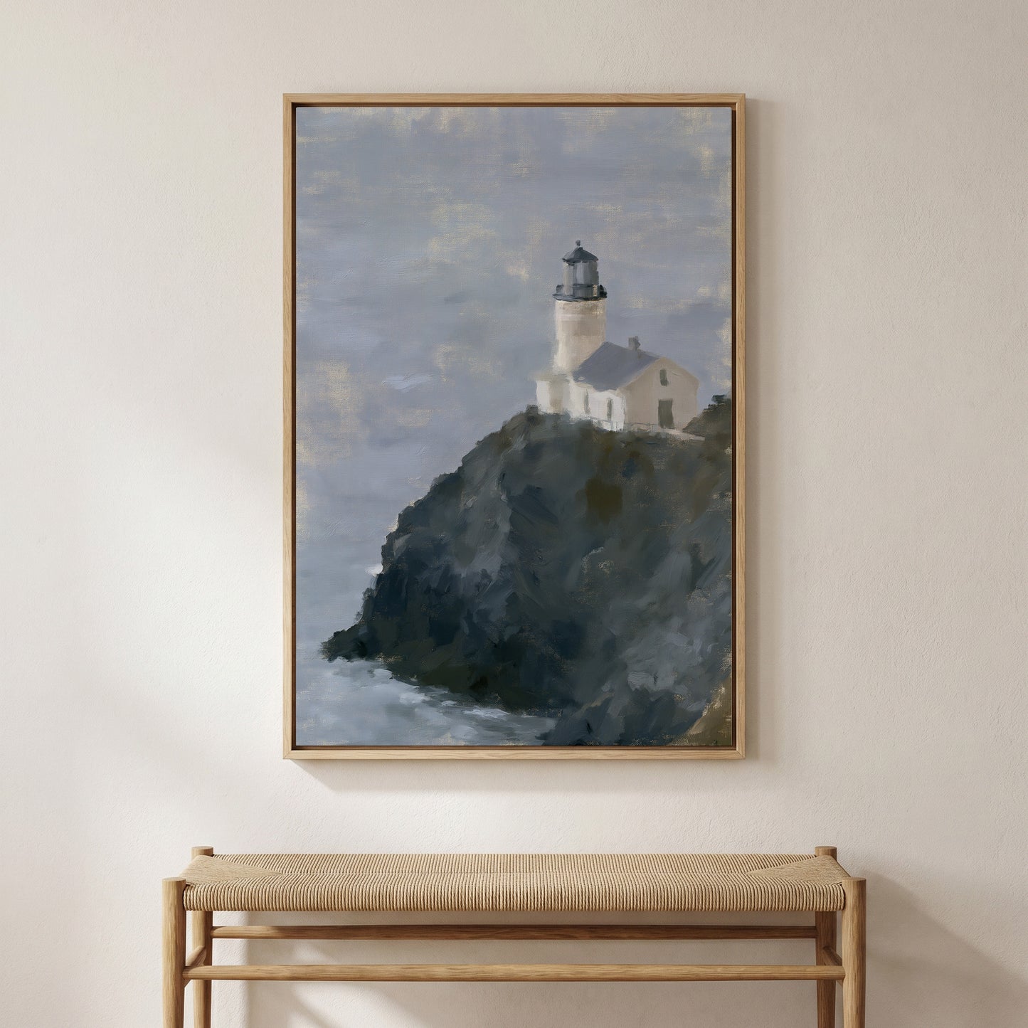 a framed painting of a lighthouse on a cliff, hanging on a wall above a bench.
