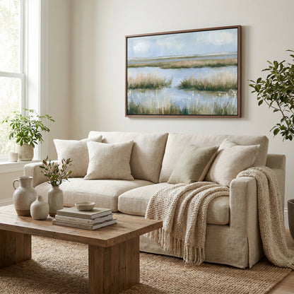 a cozy living room with a beige sofa, a wooden coffee table, and a framed landscape painting on the wall. The room is decorated with potted plants, vases, and books, creating a warm and inviting atmosphere.