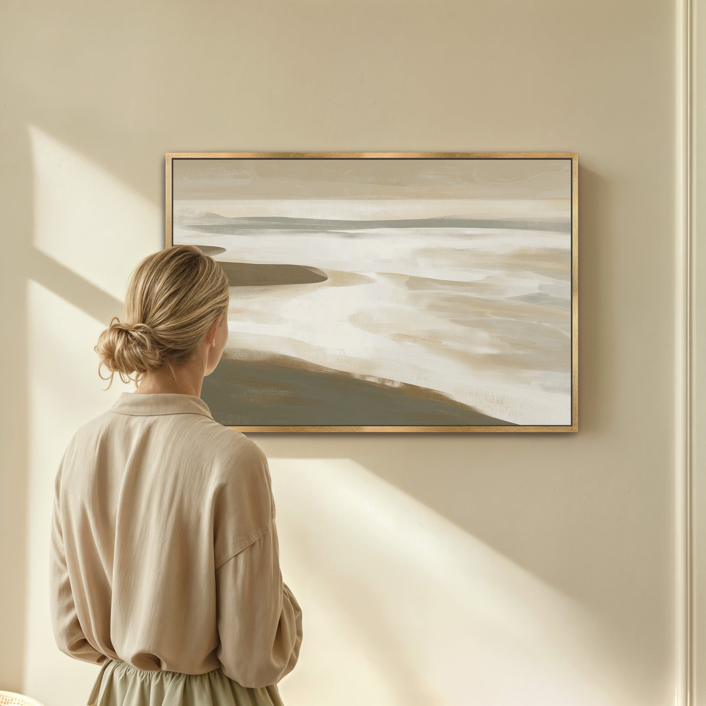 Woman viewing Emie Canvas Print of muted coastal landscape in beige and olive tones framed in gold