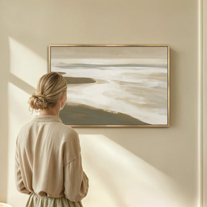 Woman viewing Emie Canvas Print of muted coastal landscape in beige and olive tones framed in gold