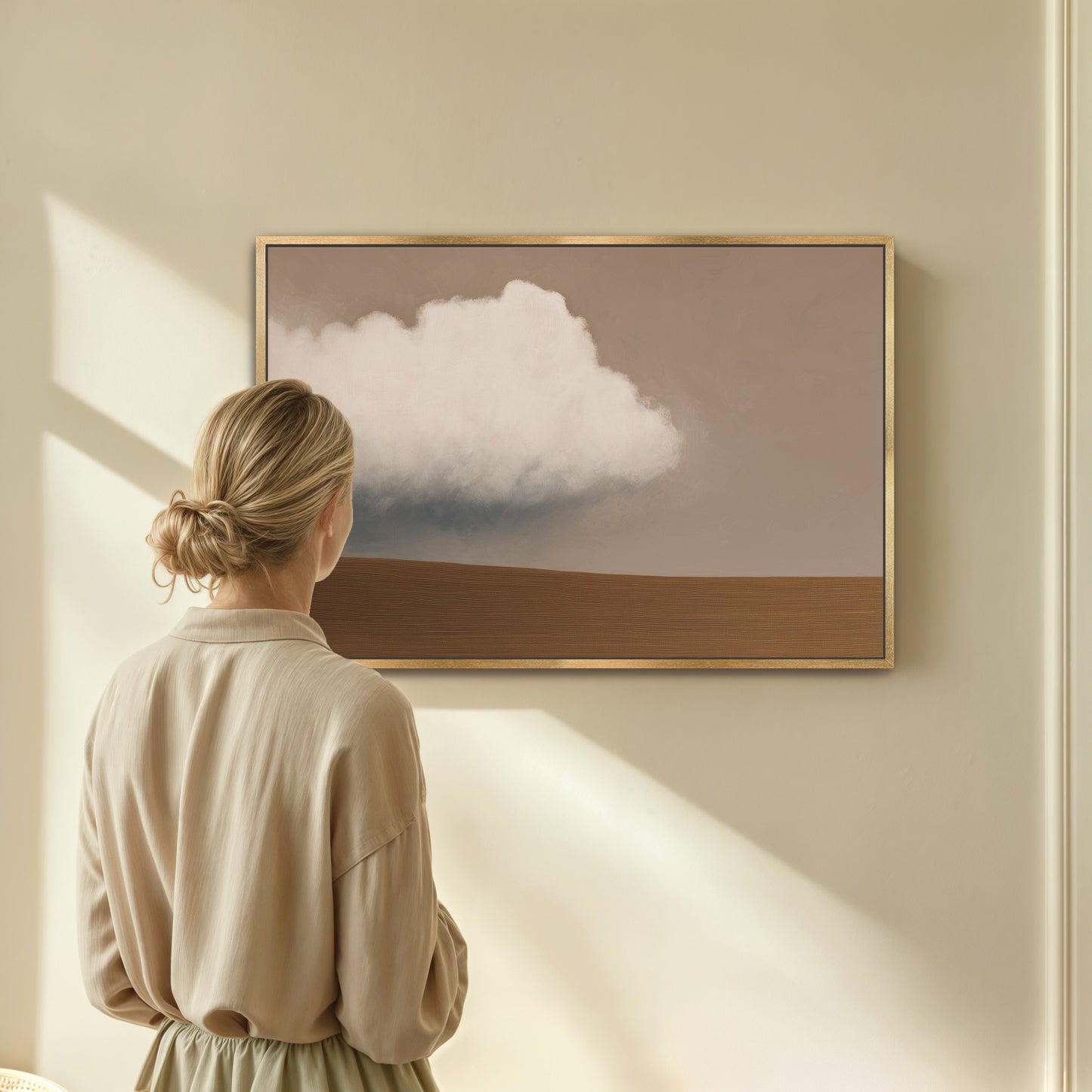 Woman viewing Aerie Canvas Print featuring minimalist cloud and earth horizon in soft taupe and ivory tones