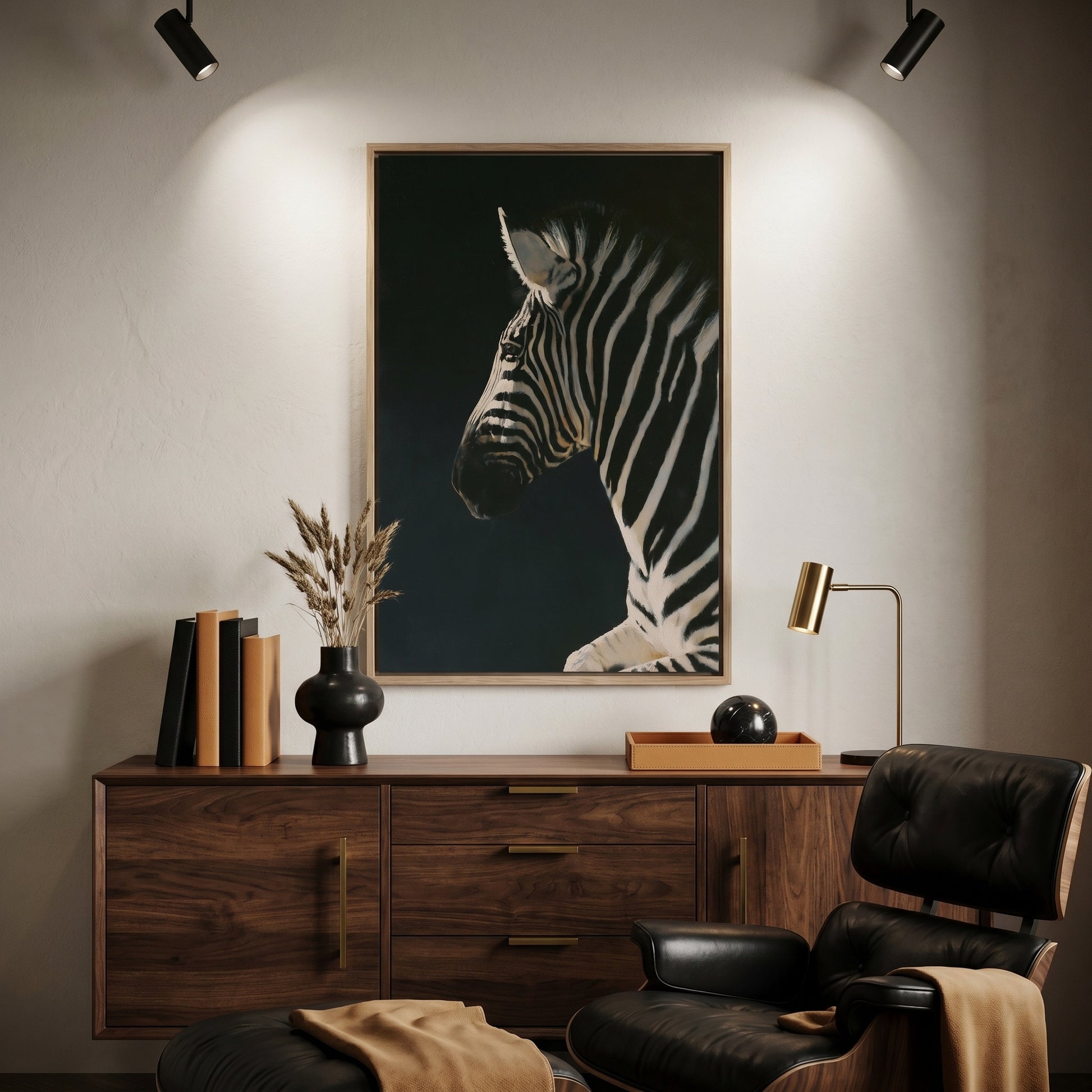 a wooden dresser with a framed painting of a zebra on it, a black leather chair, a wooden side table with a lamp, and a stack of books.