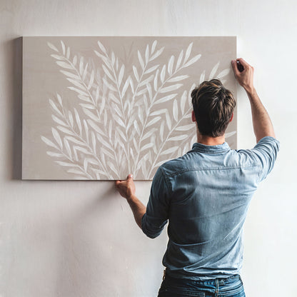 Man hanging Whisper Canvas Print with ivory leaf design on taupe background in modern room