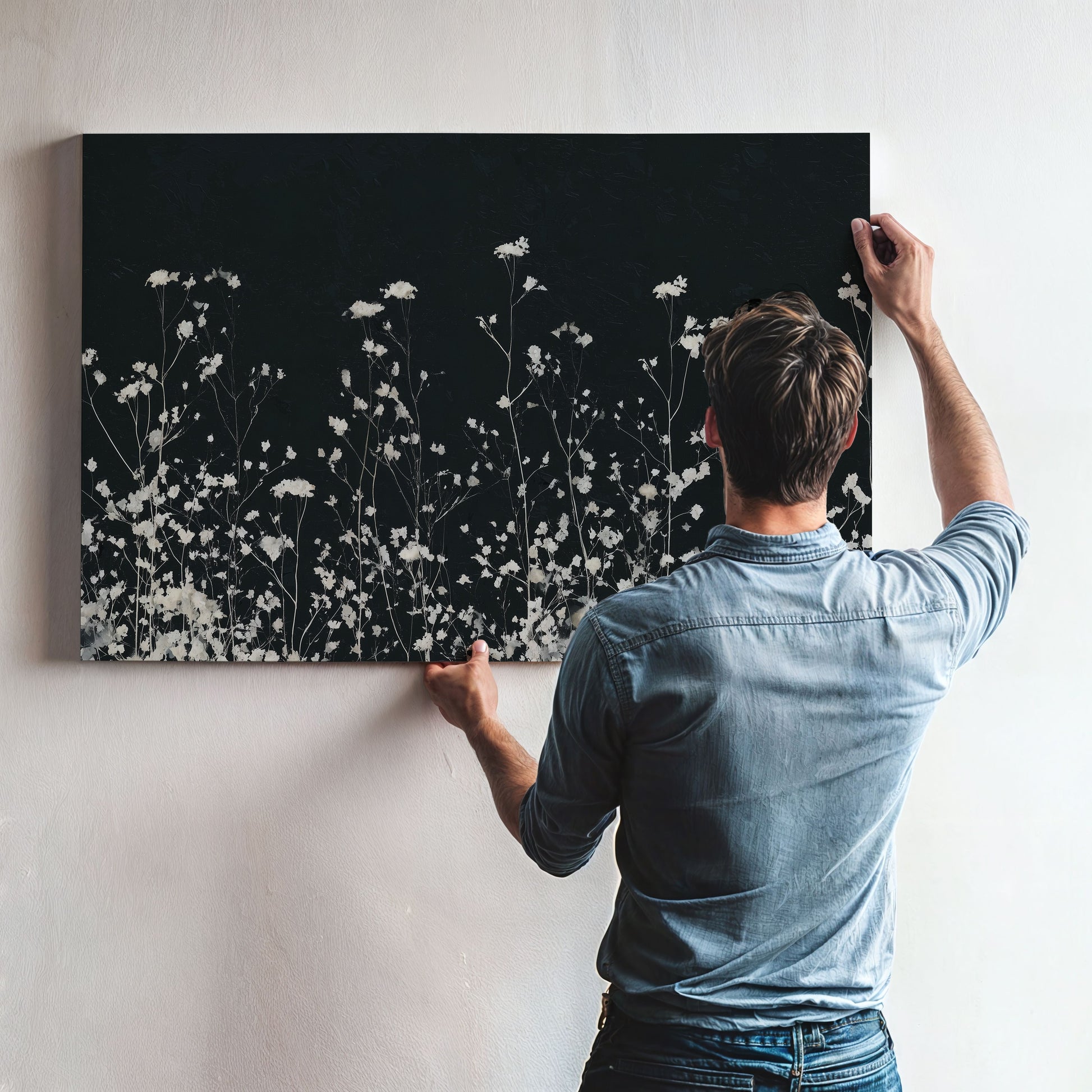 Man hanging Noiré Canvas Wall Art featuring delicate white florals on deep charcoal background