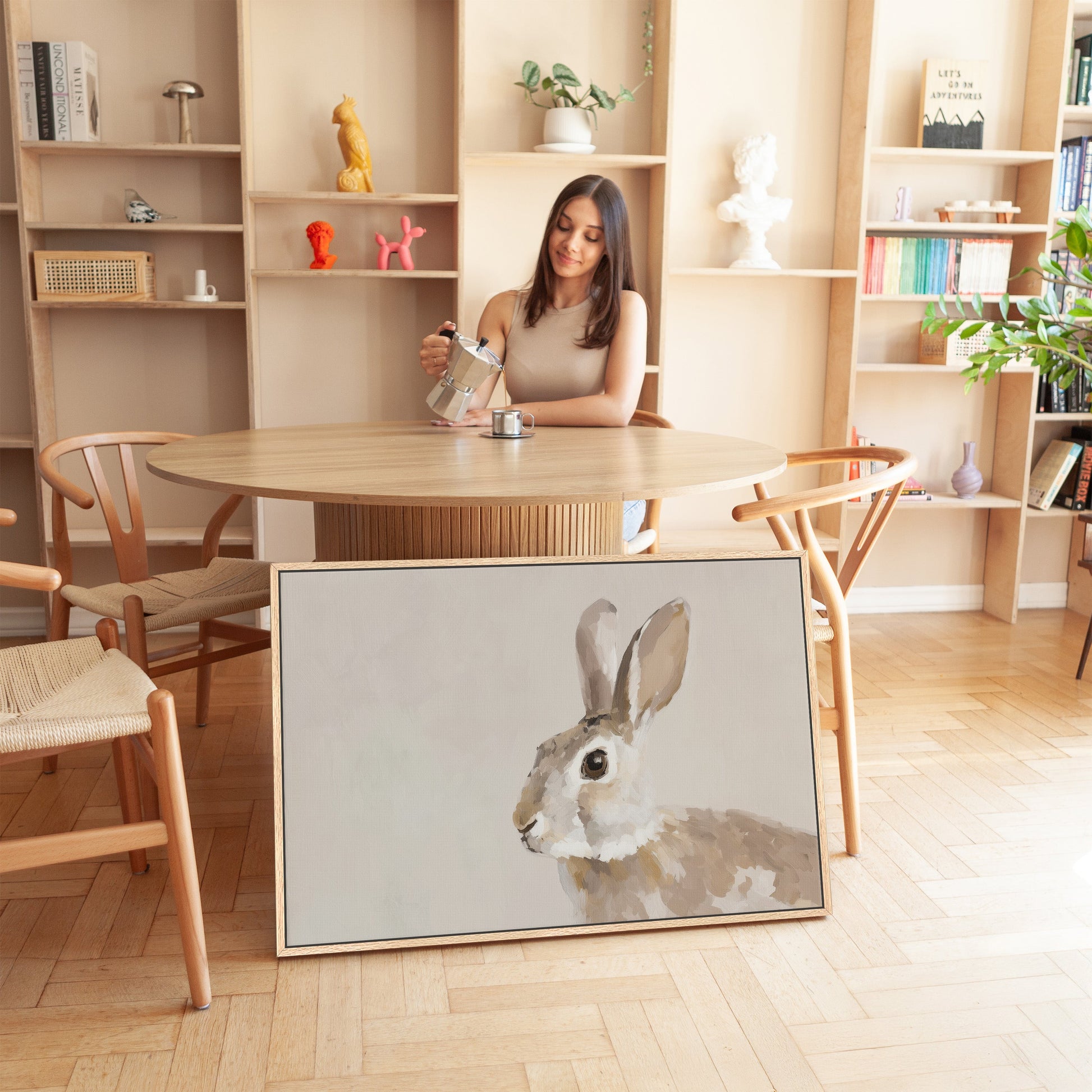 Minimalist living room with woman pouring coffee and Clover canvas print of a rabbit in soft neutrals leaning against table