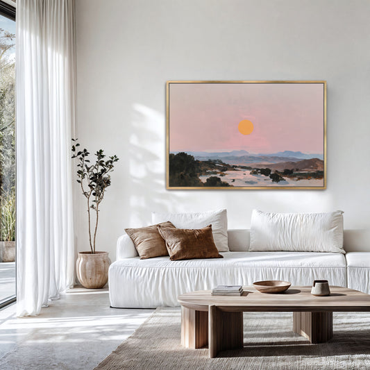 a serene living room with a white sofa, a wooden coffee table, and a large framed painting of a sunset over a mountain landscape hanging on the wall.