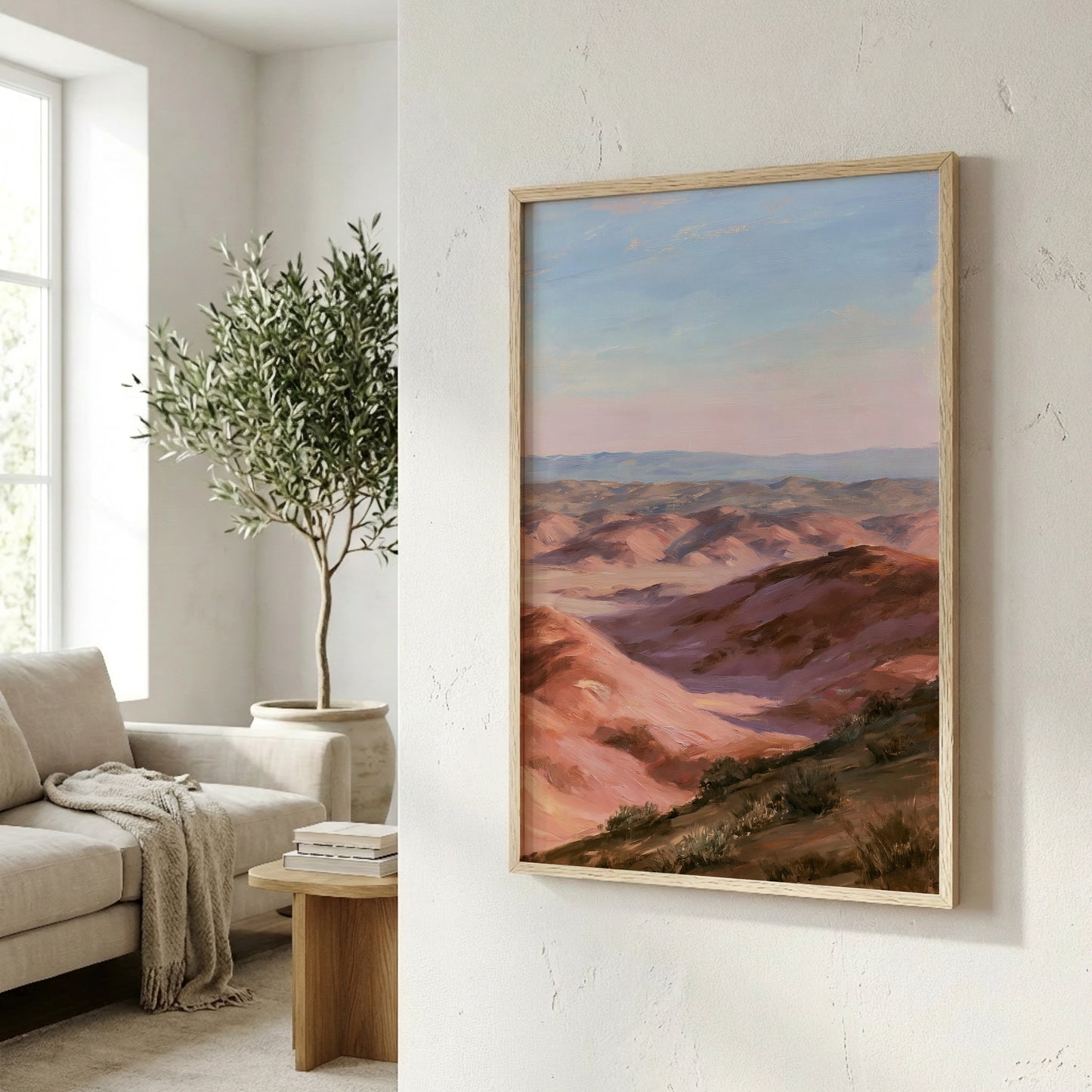 a framed painting of a mountainous landscape with a warm, reddish-brown hue, hanging on a white wall in a living room setting.