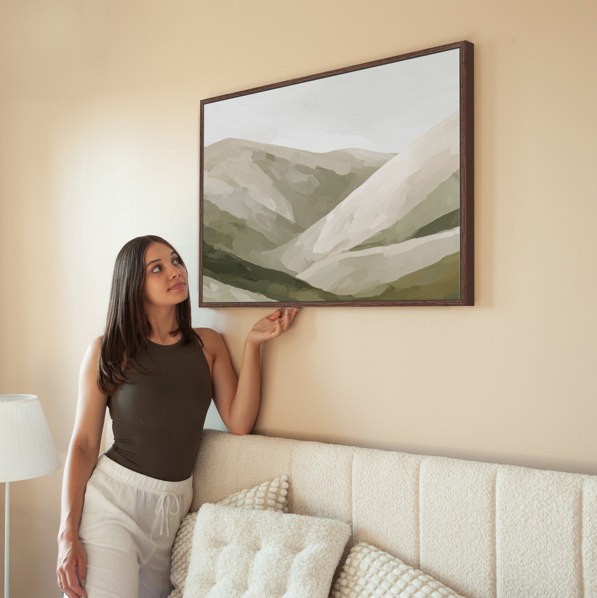 Woman admiring Olive Hills canvas print in neutral tones above a sofa