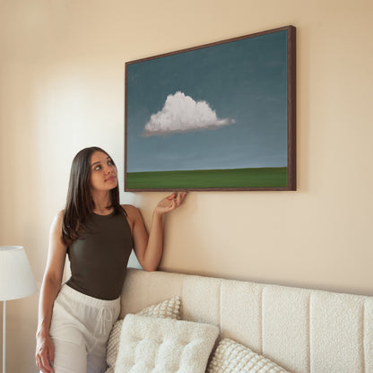 Eave canvas print with single cloud over green horizon in wooden frame hanging on beige wall