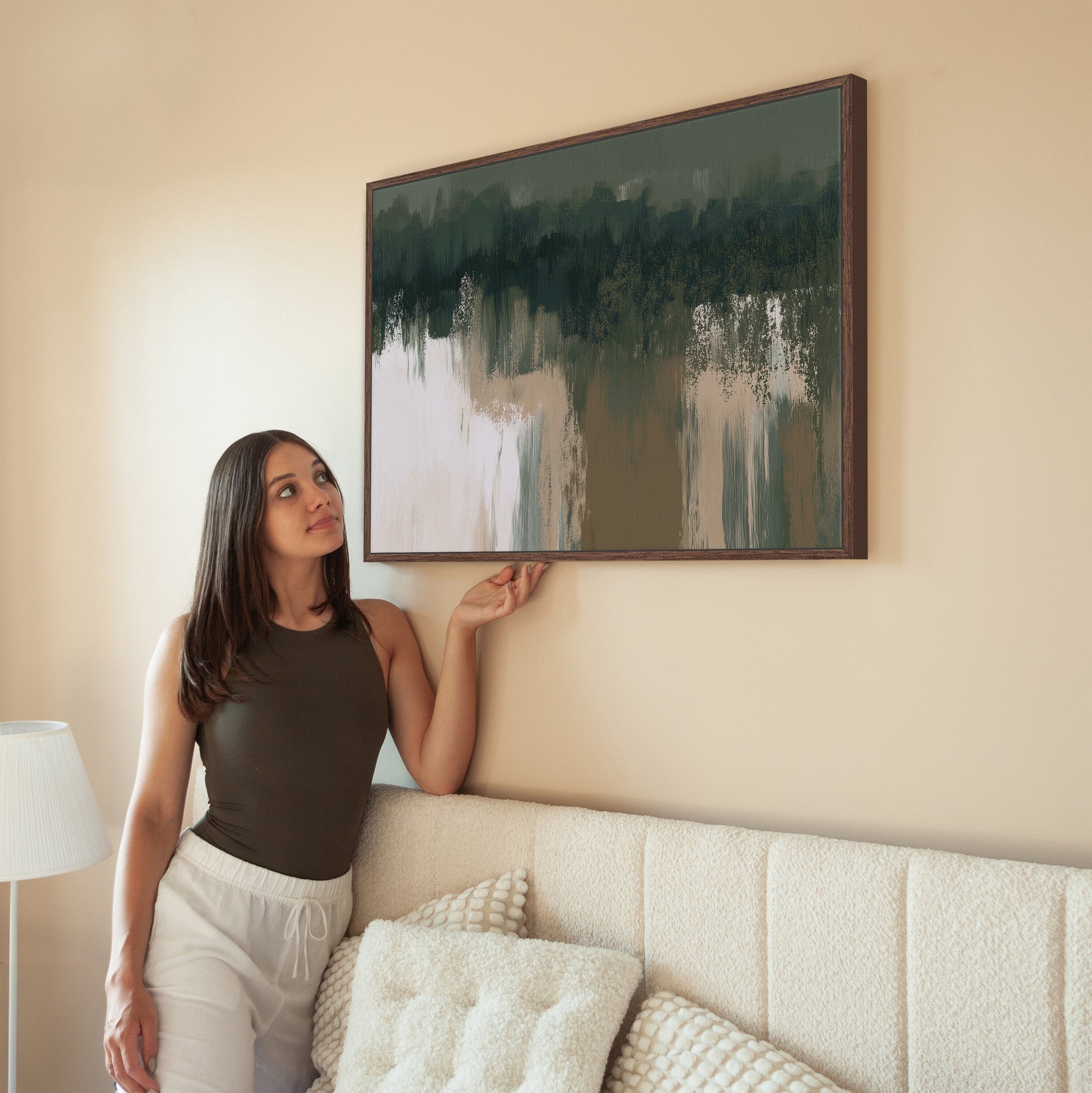 Woman hanging Forestline canvas print with green and taupe abstract forest art on beige living room wall