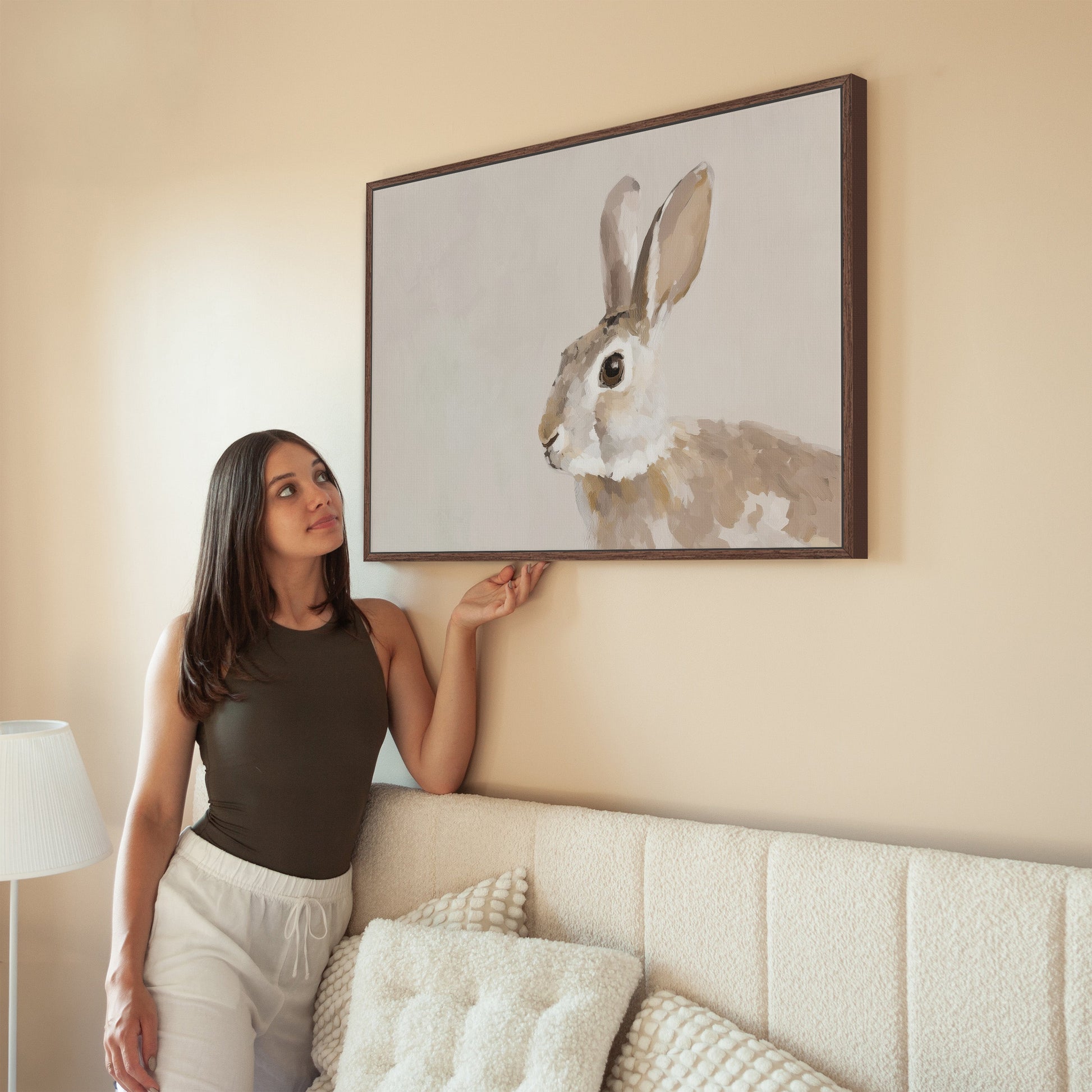 Clover Canvas Print of a serene neutral-toned rabbit hanging in a minimalist living room with a woman admiring it