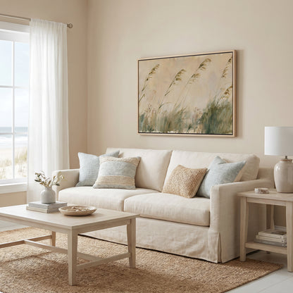 a cozy living room with a beige sofa adorned with throw pillows, a wooden coffee table, and a framed artwork of tall grasses hanging on the wall.
