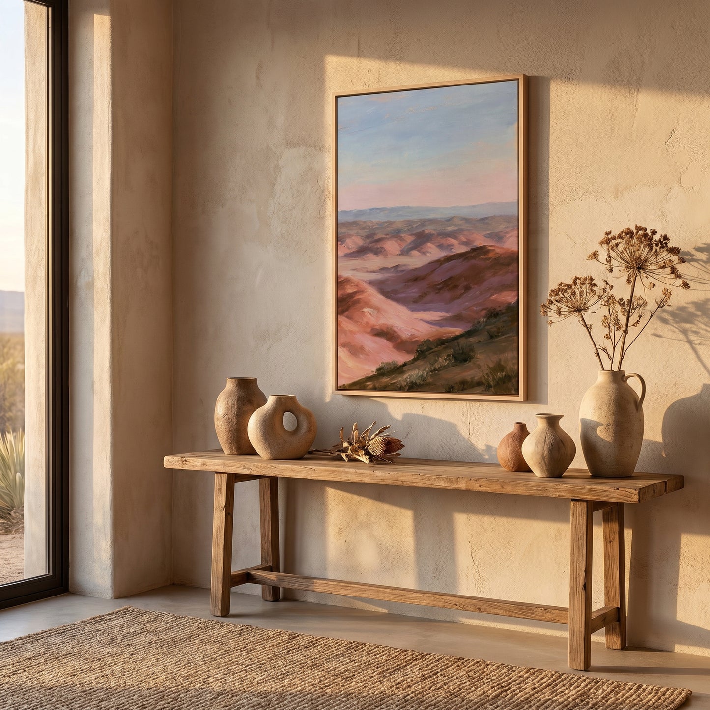 a wooden console table with three vases and a framed landscape painting hanging on the wall above it. The table is situated in a room with a large window, allowing natural light to illuminate the space.