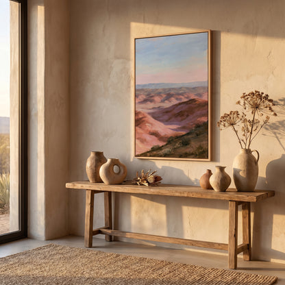 a wooden console table with three vases and a framed landscape painting hanging on the wall above it. The table is situated in a room with a large window, allowing natural light to illuminate the space.
