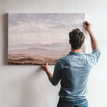 A man is hanging a large landscape painting on a wall, looking at the painting as he works.