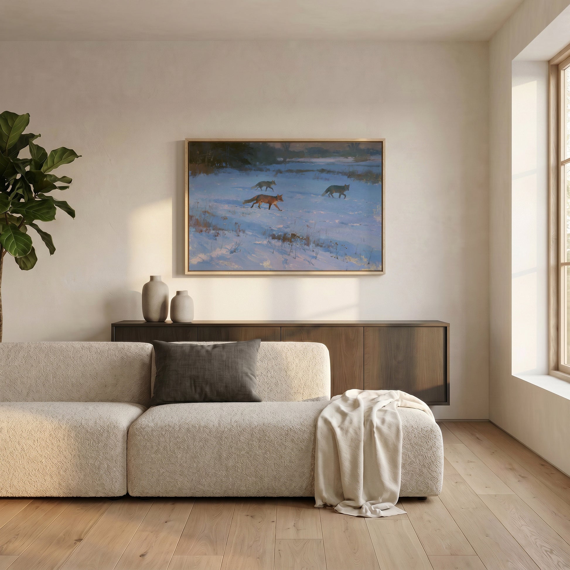 a cozy living room with a large window, a beige sofa, a wooden cabinet, and a framed painting of three foxes in a snowy landscape.