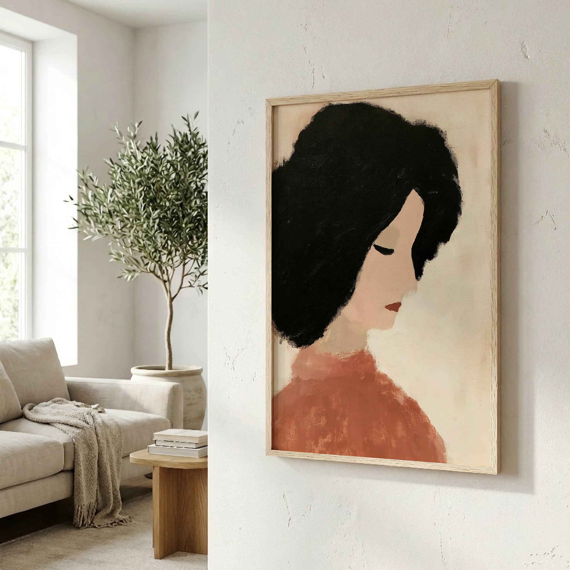 a framed portrait of a woman with black hair, hanging on a wall in a living room. The room has a white sofa, a wooden side table, and a potted plant, creating a cozy and inviting atmosphere.