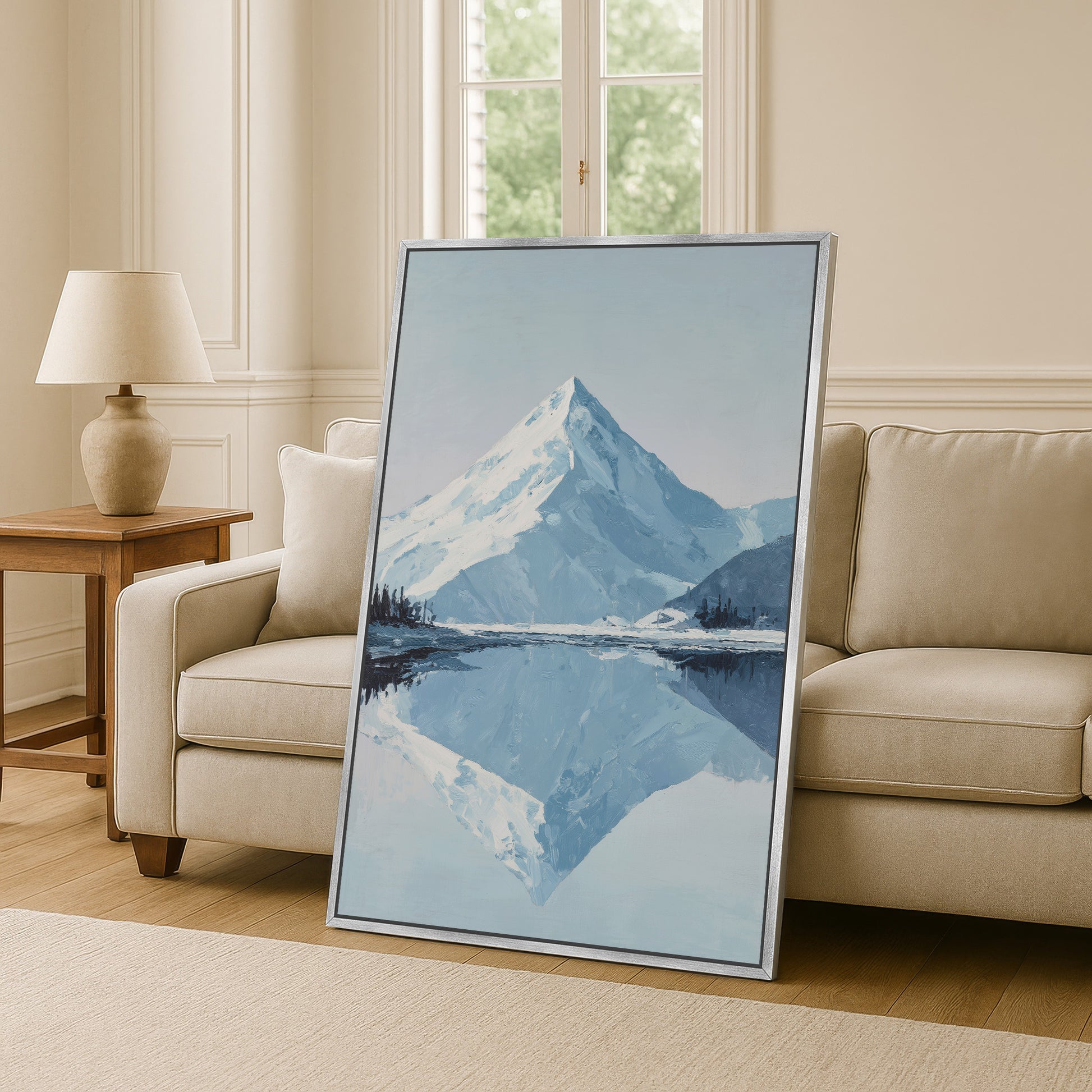 a large framed painting of a mountain landscape with a lake in the foreground, placed on a wooden floor in a living room setting.