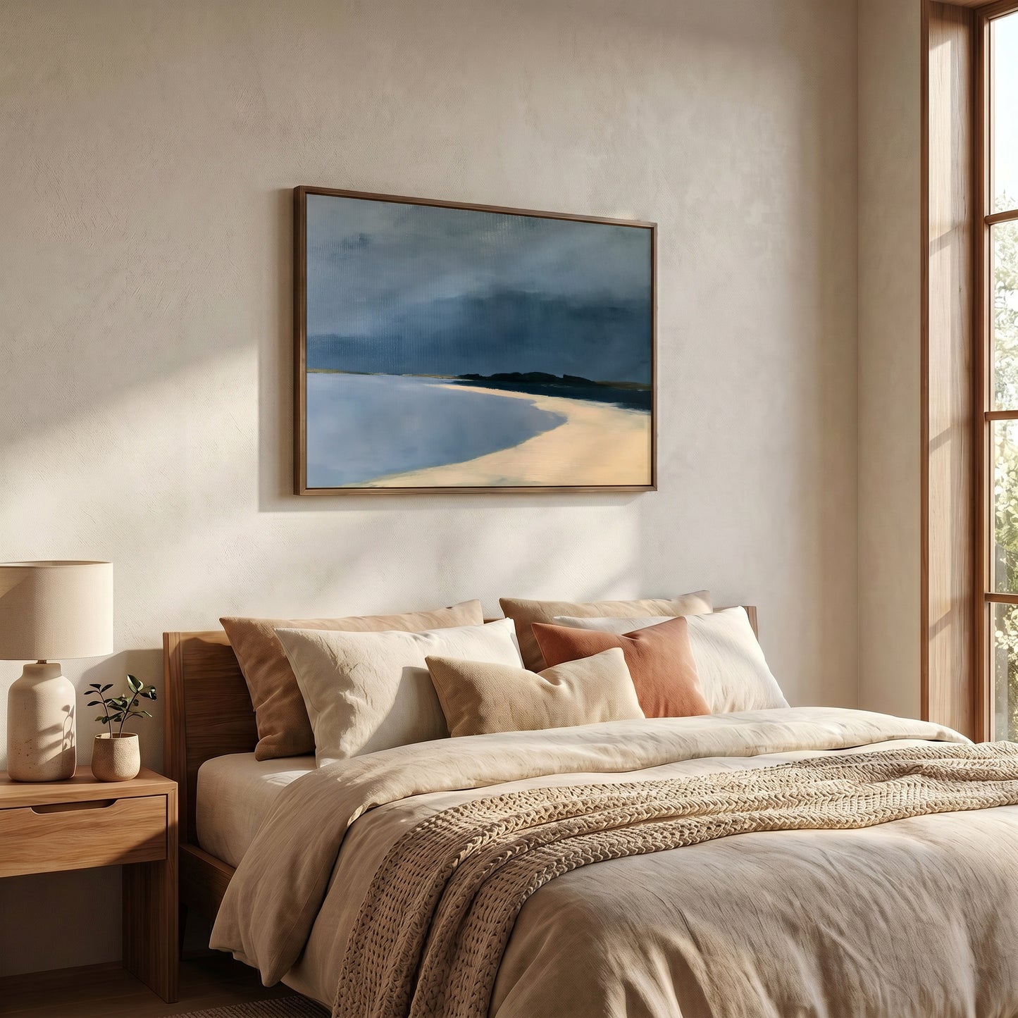 a serene bedroom scene with a large bed adorned with beige bedding and a wooden headboard. Above the bed, a framed painting of a beach landscape is hung on the wall, adding a touch of nature to the room. The room is well-lit, with natural light streaming in from a window on the right side, creating a peaceful and inviting atmosphere.