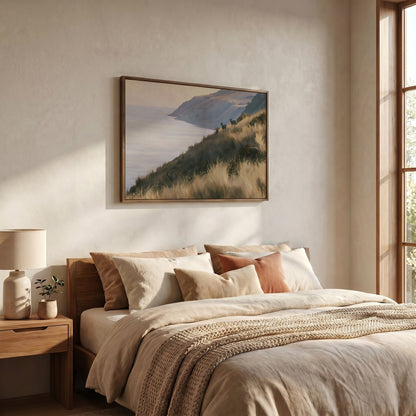 a serene bedroom scene with a large bed adorned with beige bedding and a framed landscape painting hanging above it. The painting features a mountainous coastline with a body of water, creating a tranquil and picturesque atmosphere.
