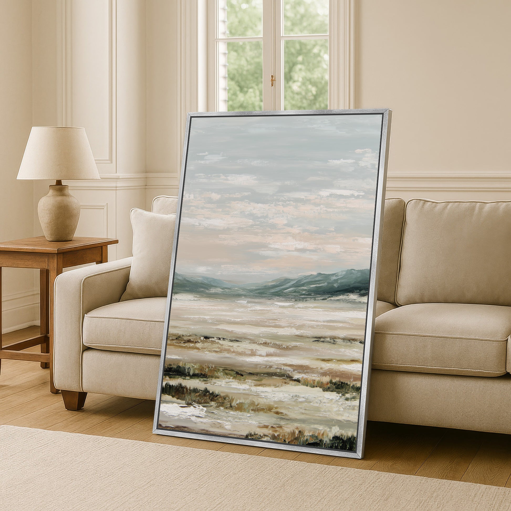 a large landscape painting displayed on a wall in a living room, with a beige sofa and a wooden side table visible in the background.