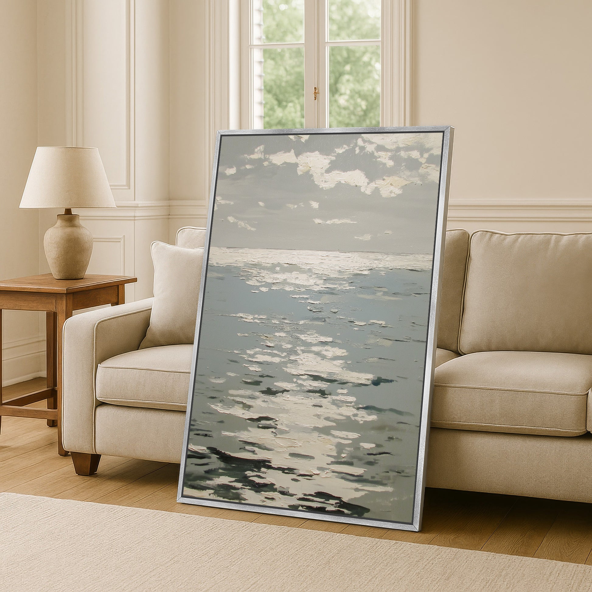 a large framed painting of a seascape, with the ocean and sky depicted in a realistic style. The painting is placed on a wooden floor in a living room setting, with a couch and a lamp visible in the background.